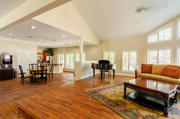 Elegant open-concept living and dining area with hardwood floors, grand piano, and abundant natural light from large windows.