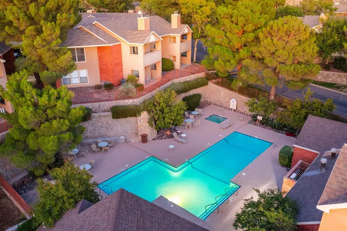 Inviting residential community with a serene outdoor pool, surrounded by lush greenery and charming multi-story homes, offering a tranquil living experience.