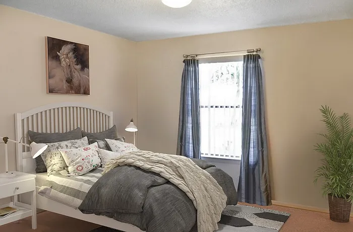 Cozy bedroom featuring a stylish bed with plush pillows, elegant bedside lamps, tranquil wall art, and natural light from a curtained window.