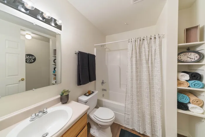 Bright and modern bathroom featuring a sleek vanity, stylish lighting, and organized shelving with colorful towels.