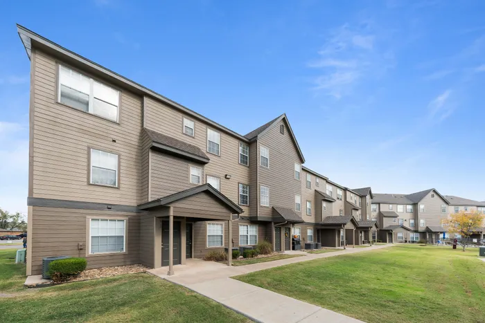 Modern three-story apartment complex with beautiful brown siding and neatly manicured lawns under a clear blue sky.