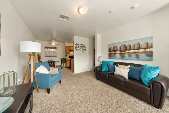 Inviting living room with modern decor, featuring a plush sofa with vibrant pillows, cozy armchair, and elegant wall art, leading into an intimate dining area and kitchen.
