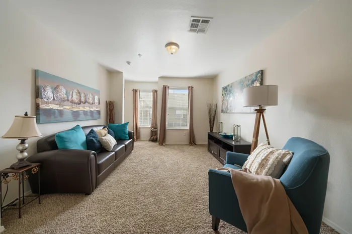 Inviting living room featuring plush carpeting, chic decor, and large windows with natural light, providing a cozy and welcoming atmosphere.