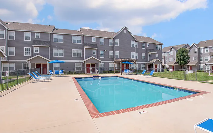 Inviting apartment complex with a refreshing outdoor pool, surrounded by comfortable lounge chairs and charming gray buildings.