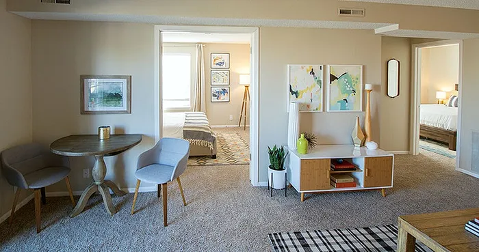 Elegant apartment interior featuring a cozy dining area with stylish chairs, vibrant wall art, and inviting bedrooms in the background.