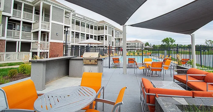 Modern apartment complex with vibrant outdoor lounge, cozy orange seating, sleek barbecue area, and inviting poolside view.