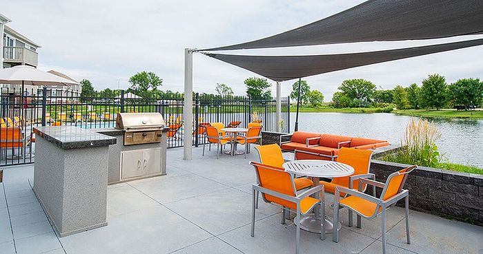 Inviting outdoor patio with vibrant orange seating, modern grill, and stunning lake view, perfect for relaxation and entertaining.