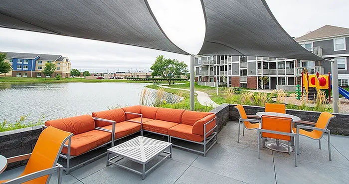 Modern outdoor lounge area with vibrant orange seating and a scenic view of a lake with surrounding greenery, ideal for relaxation.