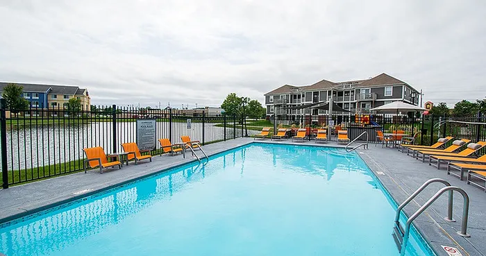 Inviting apartment complex with a sparkling pool, lounge chairs, and scenic lake views, perfect for relaxation and outdoor enjoyment.