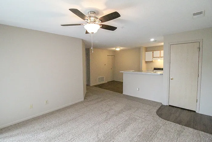Bright and spacious open-concept apartment featuring a modern living area with ceiling fan and cozy carpeted floors, seamlessly leading to a sleek kitchen.