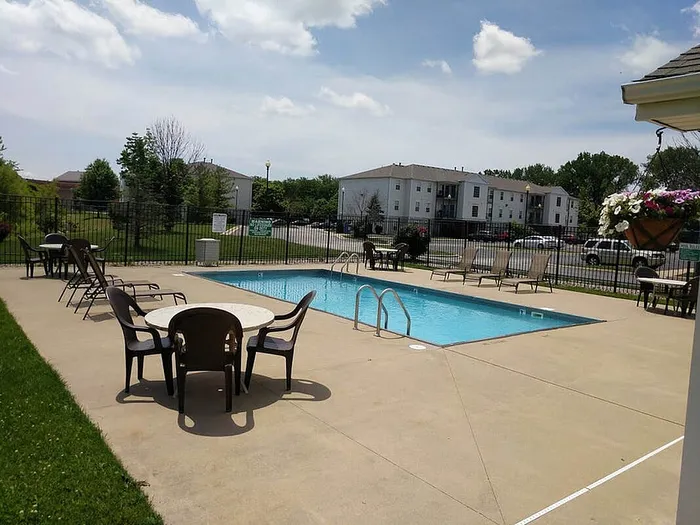Inviting outdoor pool area with elegant seating, lush surroundings, and nearby residential buildings under a clear blue sky.