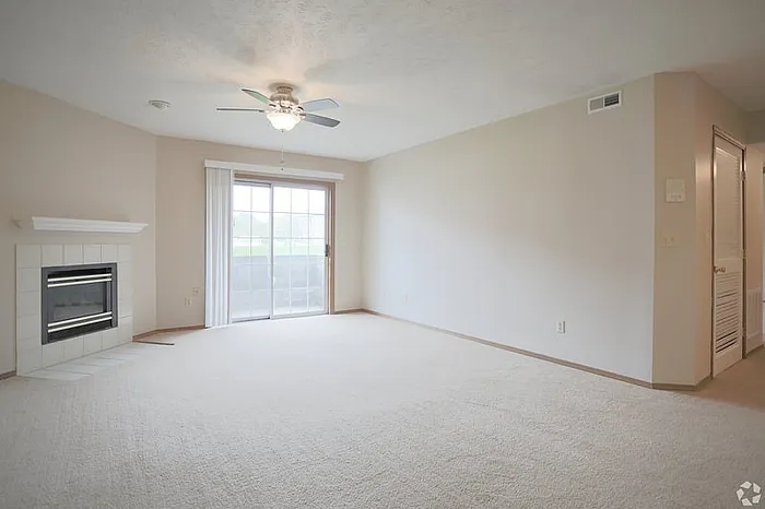 Bright and airy living room with plush carpeting, modern ceiling fan, and a cozy fireplace, opening to a serene outdoor patio through sliding glass doors.