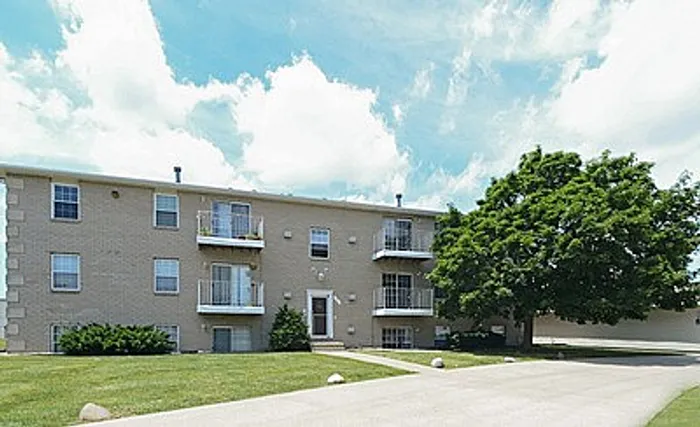 Charming apartment complex with balconies, serene greenery, and expansive outdoor space under a bright blue sky.