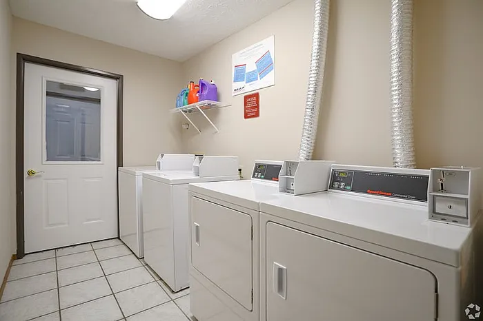Bright and spacious laundry room featuring modern washers and dryers, tiled flooring, and convenient shelving for laundry essentials.