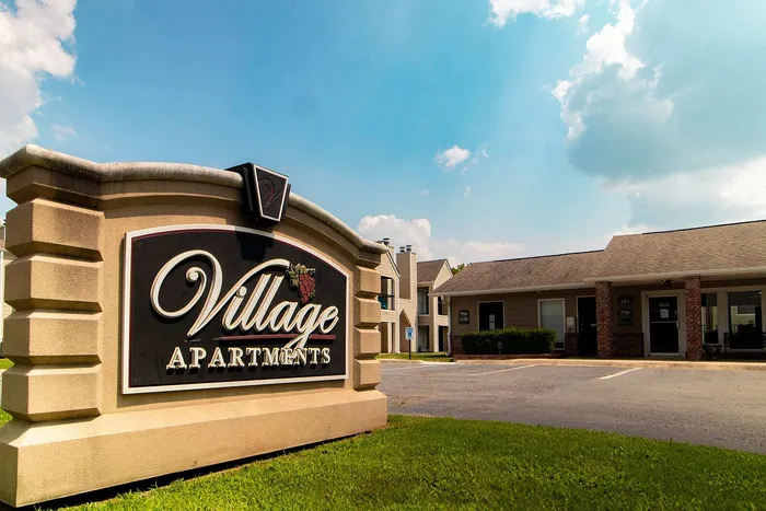Charming Village Apartments entrance with elegant sign and well-maintained landscape under a bright blue sky.