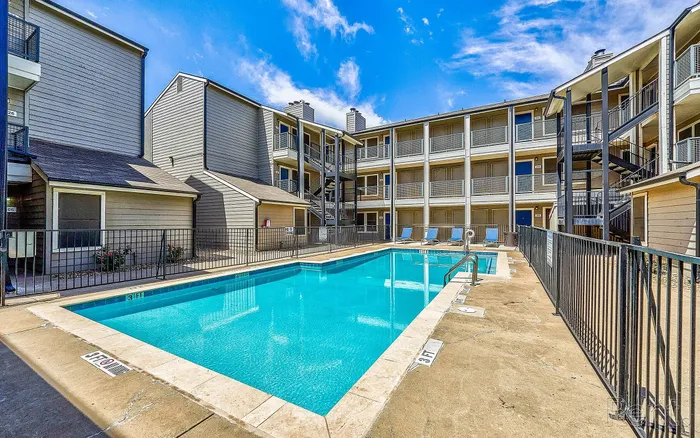 Charming apartment complex featuring a sparkling swimming pool, surrounded by sunlit windows and inviting balconies.