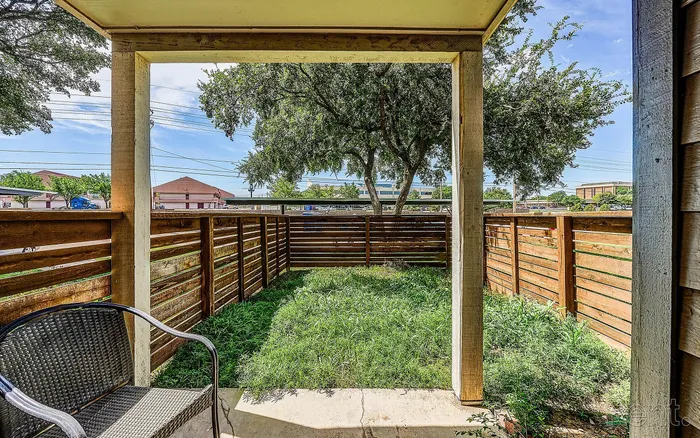 Charming patio space with cozy seating, enclosed by a wooden fence, offering a lush green view under the open sky.