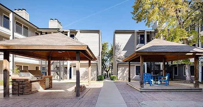 Inviting apartment courtyard featuring two stylish gazebos, modern outdoor grill area, and comfortable seating under clear blue skies.