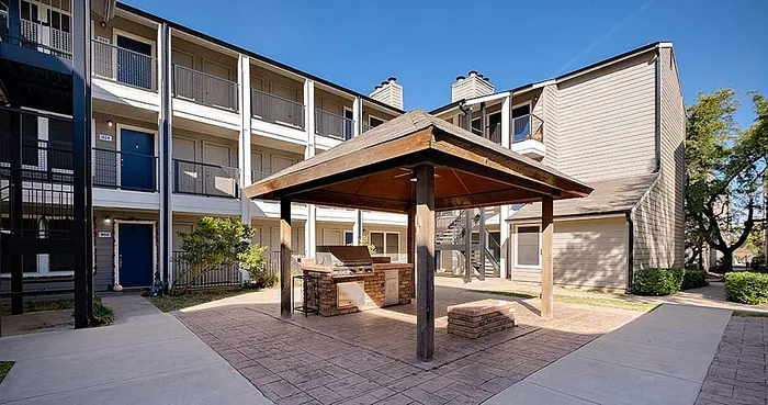 Charming apartment complex with a central gazebo and built-in barbecue area, surrounded by lush greenery and modern architecture.