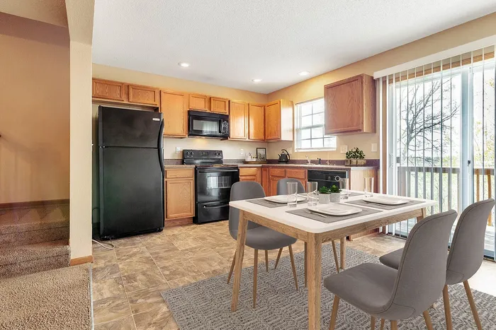Charming kitchen and dining area featuring modern appliances, oak cabinetry, and a sunlit glass door leading to a serene view.