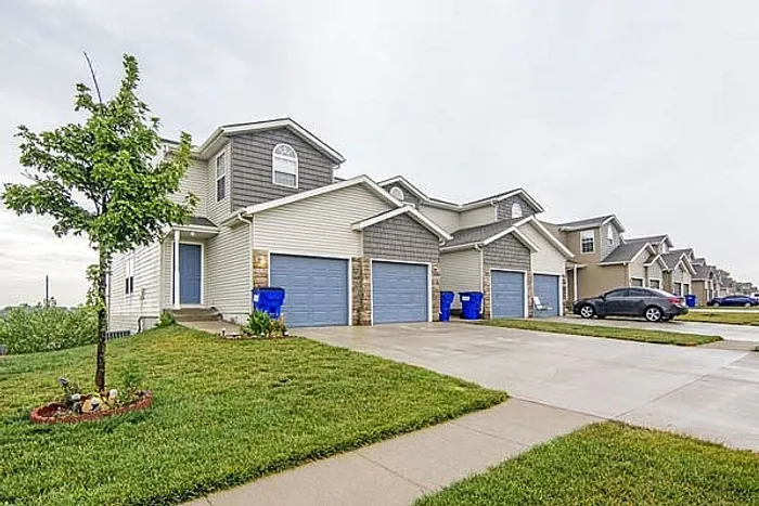 Charming row of modern two-story homes with blue garages, well-maintained lawns, and a serene suburban setting.