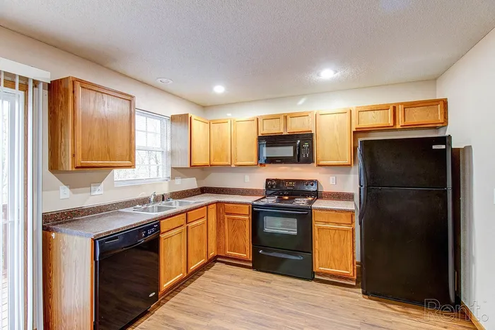 Inviting kitchen with warm wooden cabinetry, sleek black appliances, and beautiful hardwood floors.
