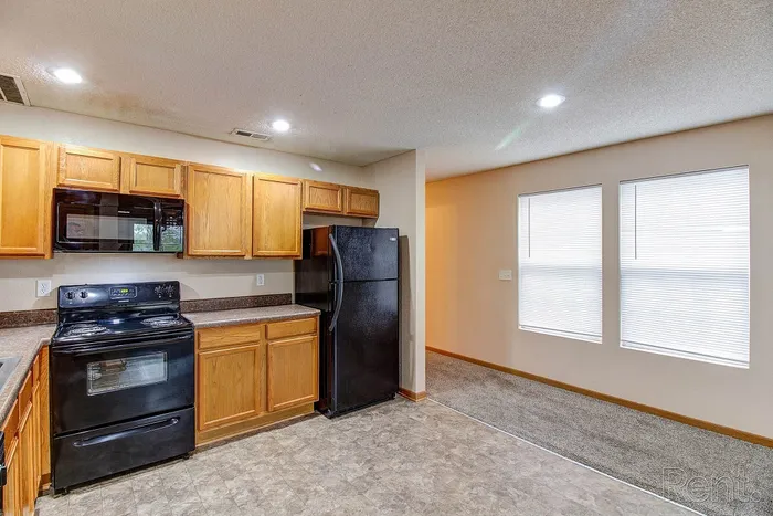 Bright kitchen with wooden cabinets, sleek black appliances, and large windows offering natural light.