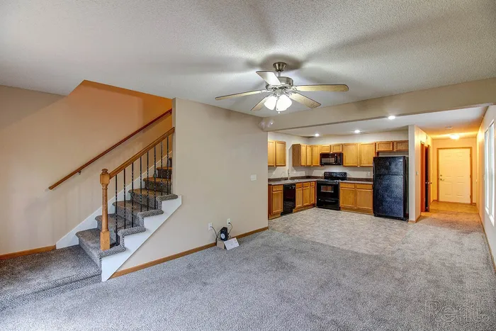 Inviting living space with open kitchen, modern appliances, and cozy carpeted staircase.