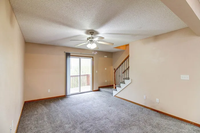 Inviting living room with plush carpet, elegant ceiling fan, and sliding glass doors leading to a charming balcony with scenic views.