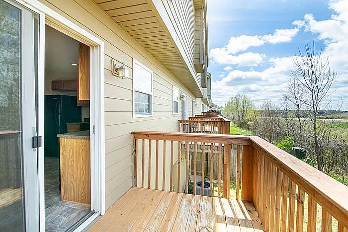 Charming apartment balcony with wooden railing, offering scenic views of lush greenery and a bright, sunny sky.