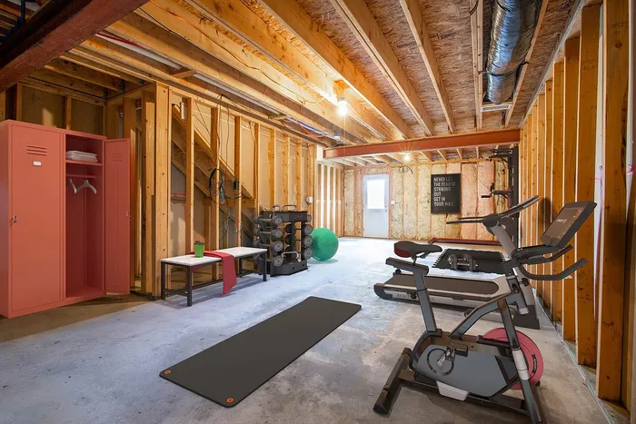 Inviting home gym in a rustic wooden basement featuring a treadmill, exercise bike, yoga mat, and vibrant red locker.
