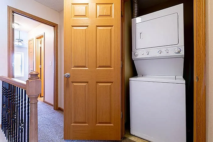 Cozy interior hallway featuring a convenient in-unit laundry with a stackable washer and dryer behind a wooden door.