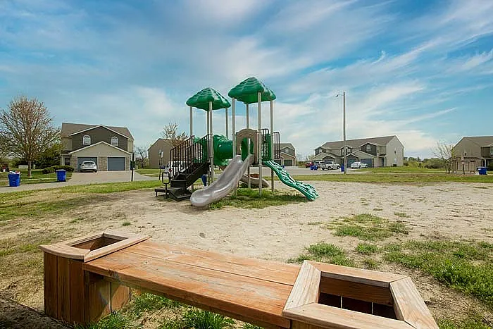 Charming neighborhood playground with vibrant green slides, set against a backdrop of cozy suburban homes and a bright blue sky.