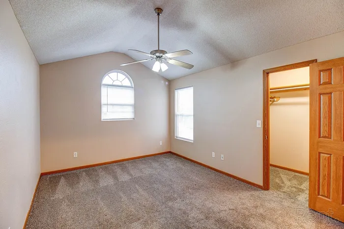 Bright, spacious bedroom with vaulted ceiling, featuring a modern ceiling fan, large closet, and arched window for natural light.
