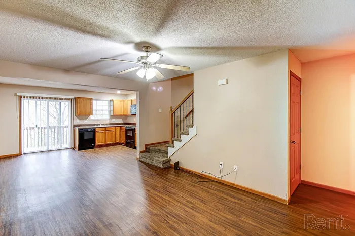 Inviting open-plan living space featuring sleek wood flooring, modern ceiling fan, and a bright kitchen area with ample cabinetry.