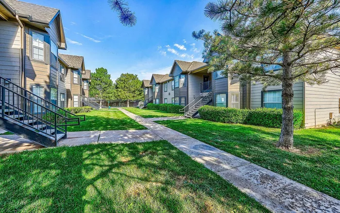 Charming apartment complex with modern two-story units, surrounded by lush greenery and well-maintained pathways.