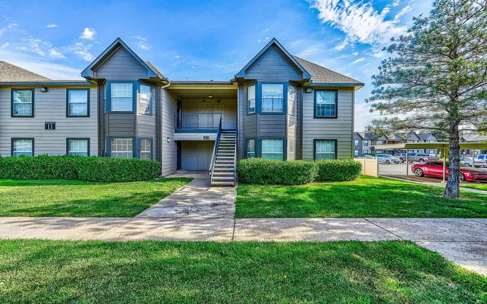 Charming two-story apartment complex with inviting landscaped greenery, set against a clear blue sky, offering modern and comfortable living.
