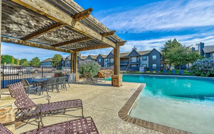 Inviting outdoor oasis featuring a sparkling pool, shaded pergola, and comfortable lounge chairs surrounded by lush greenery.