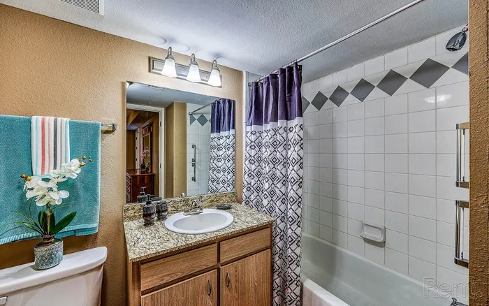 Elegant bathroom featuring a granite countertop, stylish vanity mirror, and chic patterned shower curtain.