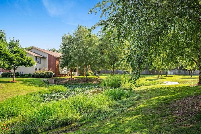 Charming residential building nestled in lush greenery with a serene pond, offering tranquil living and beautiful natural surroundings.
