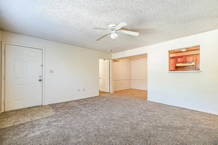 Inviting open-concept living room with plush carpeting, ceiling fan, and seamless access to cozy dining area; perfect for entertaining.