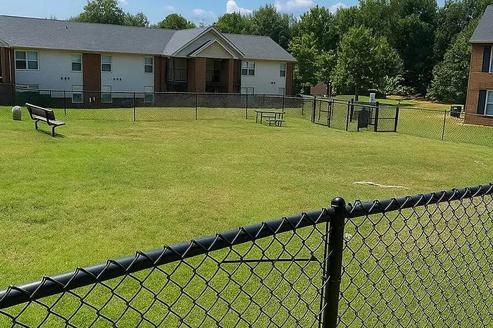 Charming green space with picnic area and benches, adjacent to a stylish apartment building, perfect for outdoor relaxation.