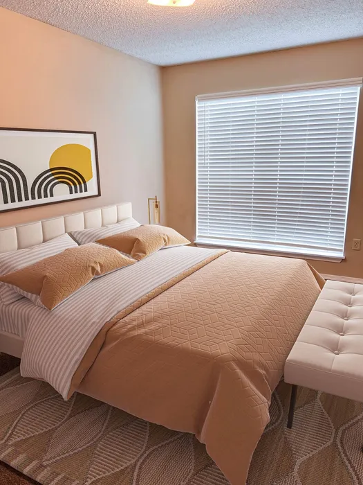 Warm and inviting bedroom with modern decor, featuring a cozy beige bed, abstract wall art, and ample natural light from large windows.