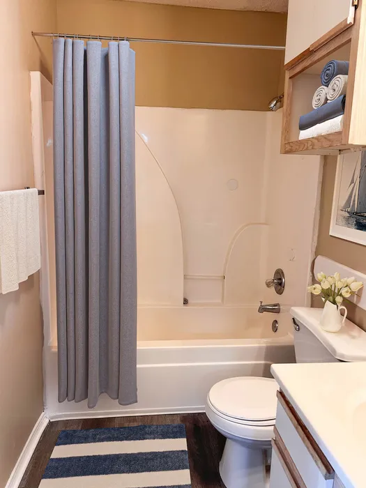 Inviting bathroom with a modern bathtub, elegant gray shower curtain, and decorative shelf with neatly folded towels.
