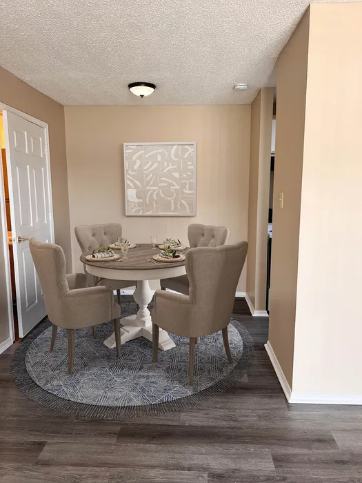Elegant dining nook with a round wooden table, four plush chairs, and chic wall art in a cozy apartment setting.