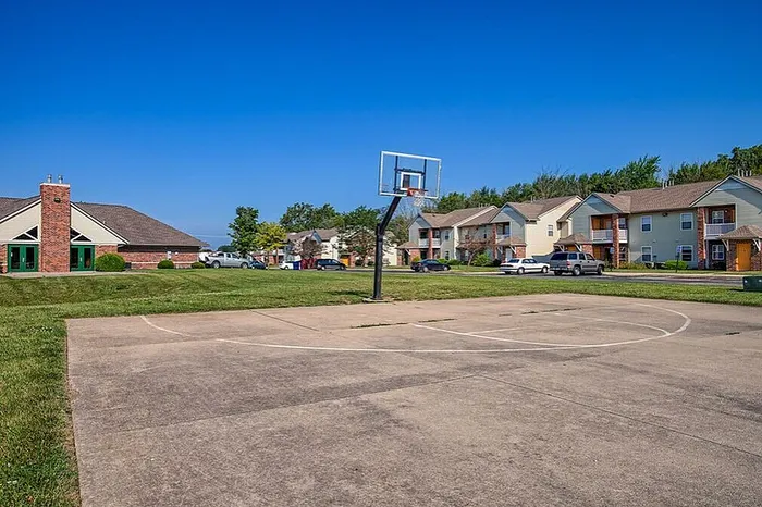 Apartment complex with charming brick accents, lush greenery, and an inviting basketball court under a clear blue sky.