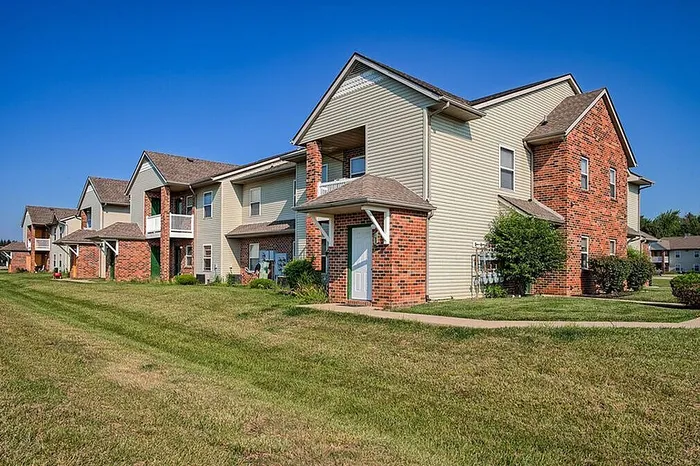Charming suburban apartment complex featuring modern brick and siding design, lush green lawns, and inviting pathways under a clear blue sky.