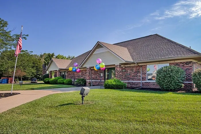 Charming brick single-story building with colorful balloons and lush greenery, perfect for a welcoming community setting.