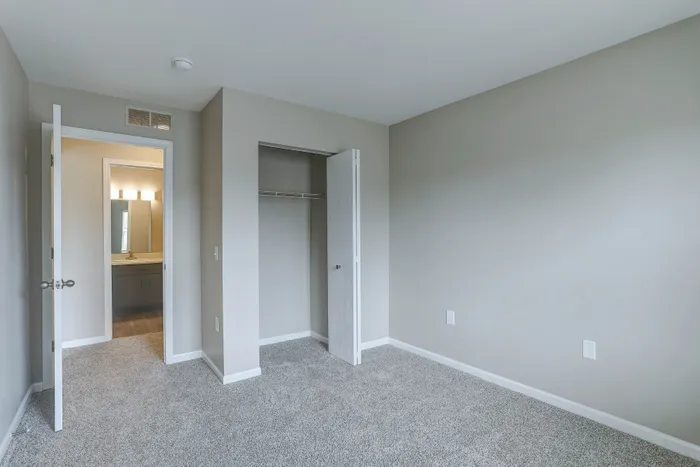 Bright, newly renovated bedroom with plush carpet, open closet, and view of modern bathroom.