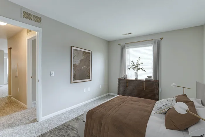 Inviting bedroom with cozy brown bedding, elegant decor, and abundant natural light from a large window.